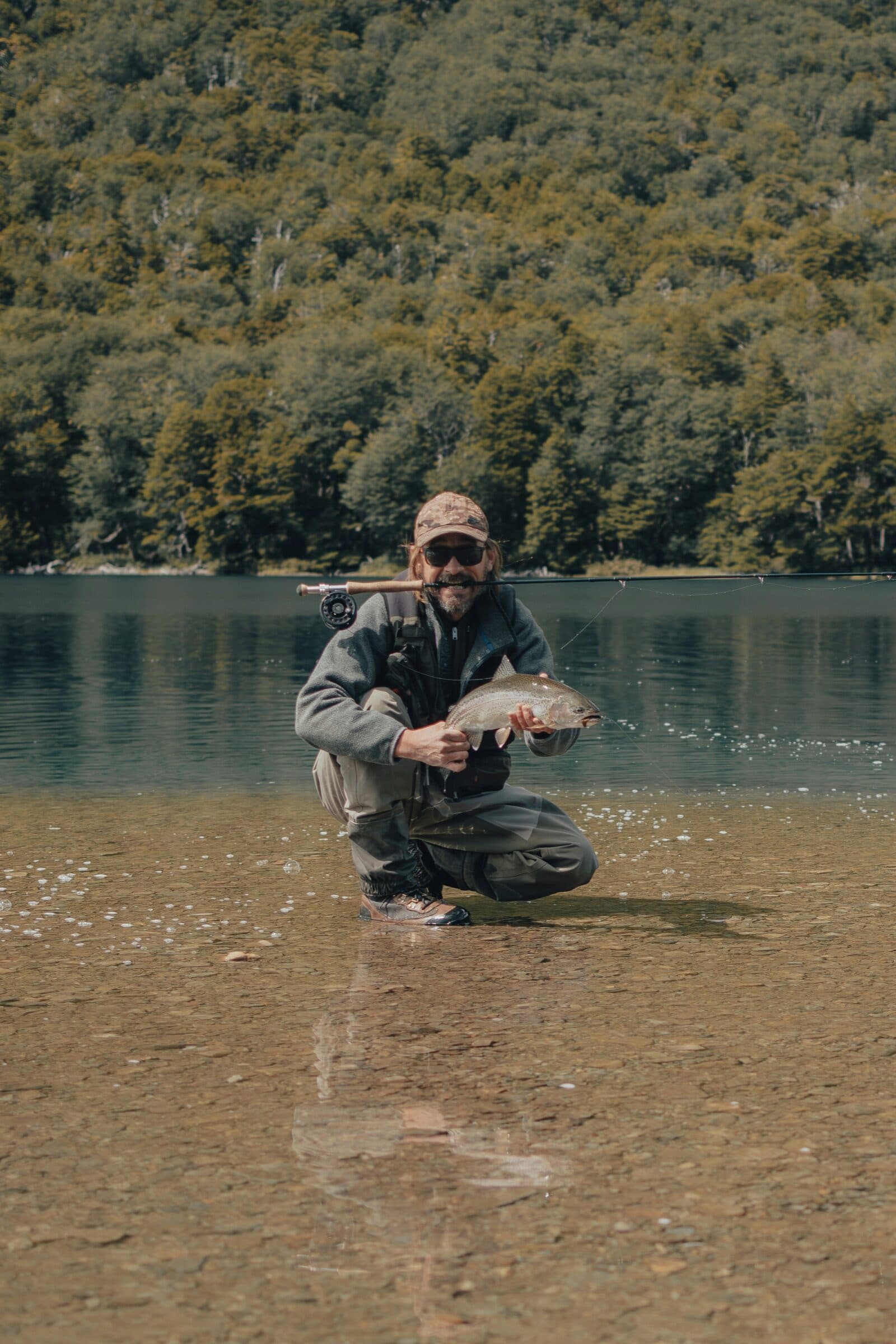 Collective member kneeling in clear water holding a rainbow trout
